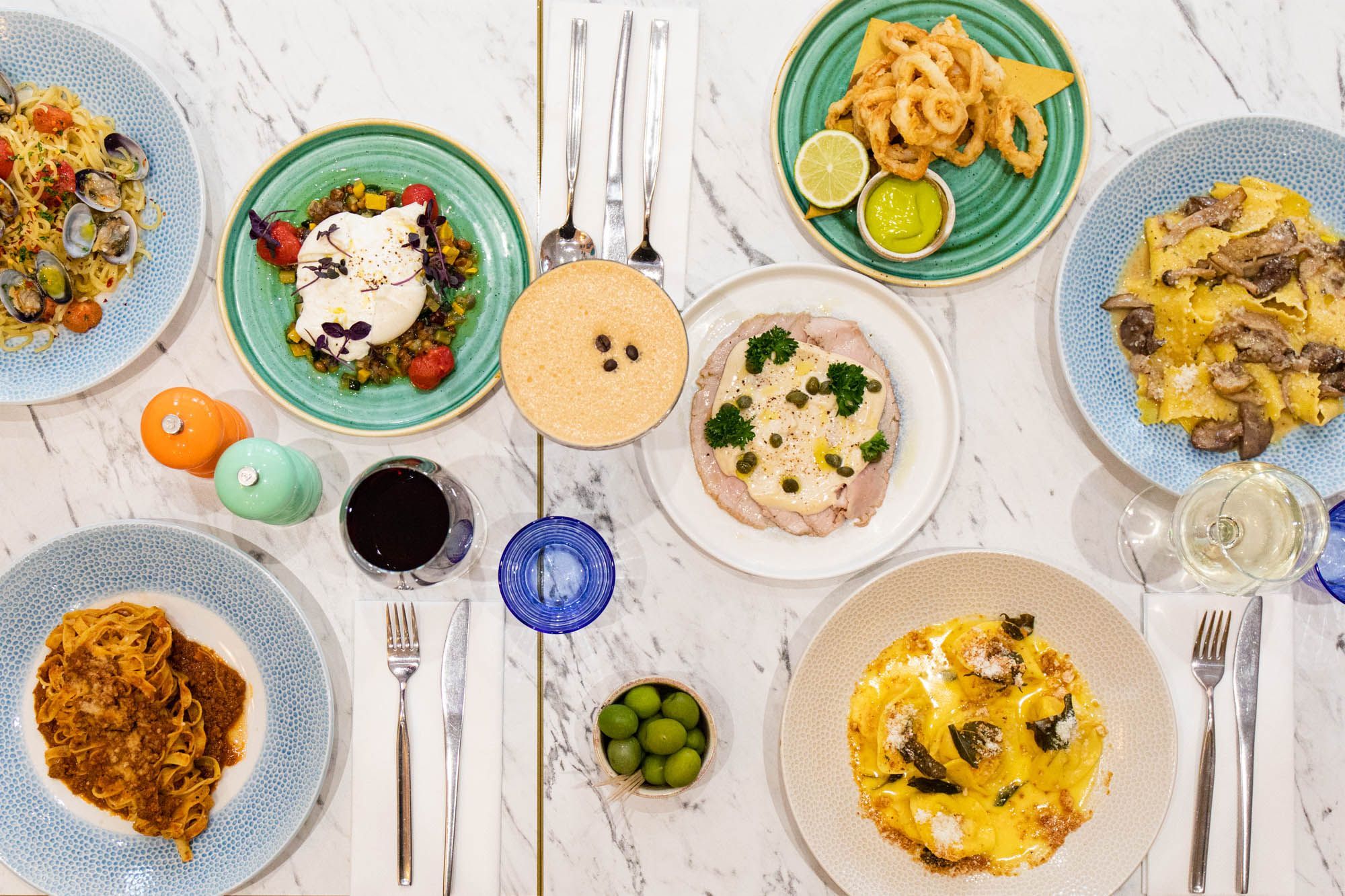 over head shot of the white table laid our with Italian dishes including different types of pasta, served with drinks