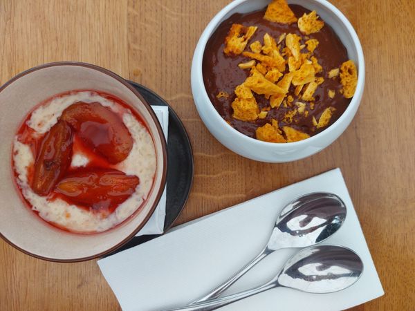 A bowl of chocolate mousse with honeycomb and a deep bowl of rice pudding with roasted plumbs