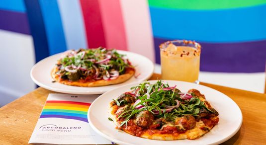 side shot of the wooden table laid out with two small pizzas, rainbow background