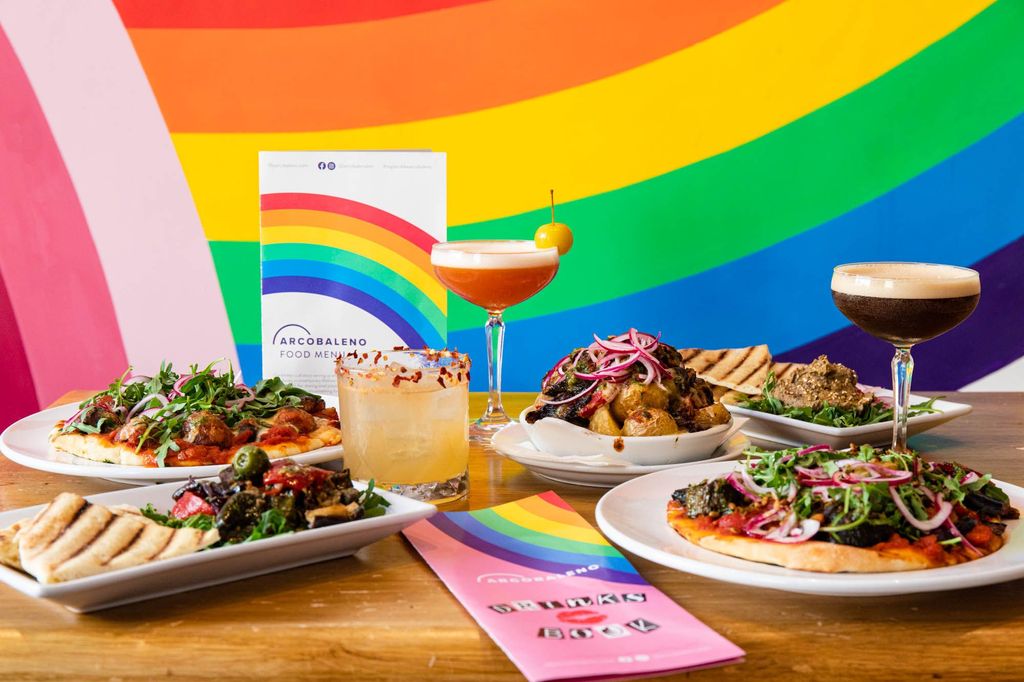 side shot of the colorful table filled with plates of food and glasses of cocktails, rainbow background