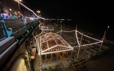 A view down onto a temporary marquee decorated with fairy lights and inside there are benches.