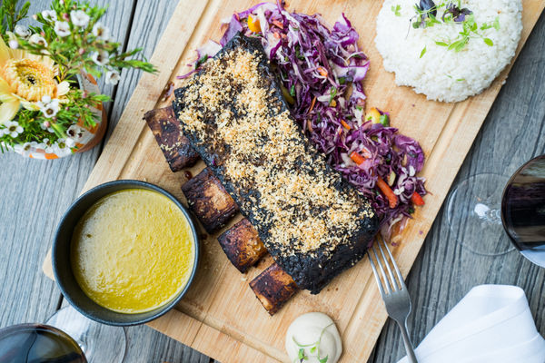 Food wooden platter with bbq ribs with a dipping sauce and red cabbage slaw and rice.