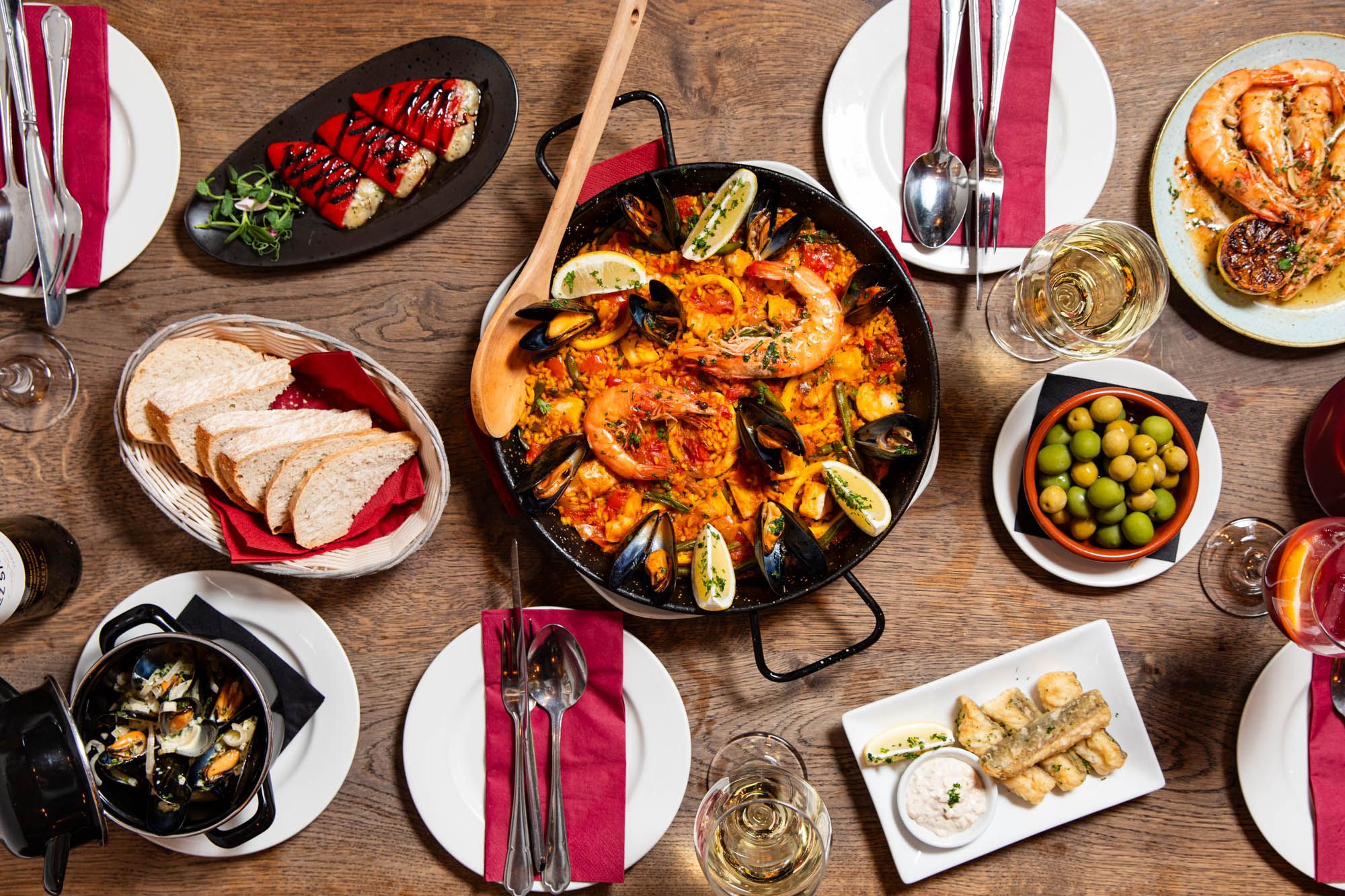 over head shot of the table laid out with delicious Spanish tapas including paella, fish dishes, bread, olives, fried fish, glasses of white wine