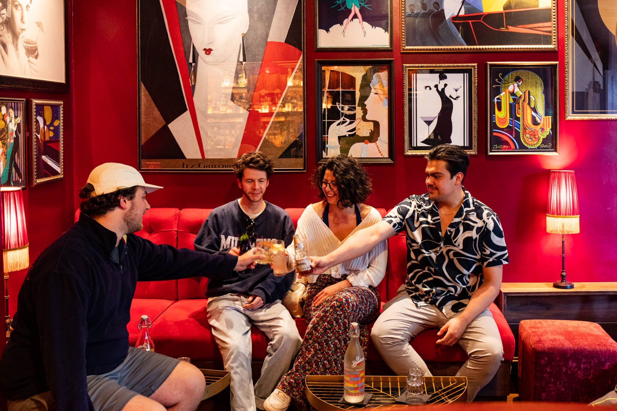 four people sitting inside the bar Valentino and having a toast, interior is decorated with many photos on their red walls