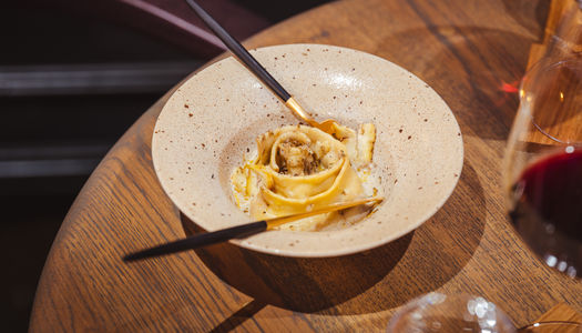 Mushroom agnolotti in a deep bowl with long armed cutlery with blue wooden handles and gold coloured utensils