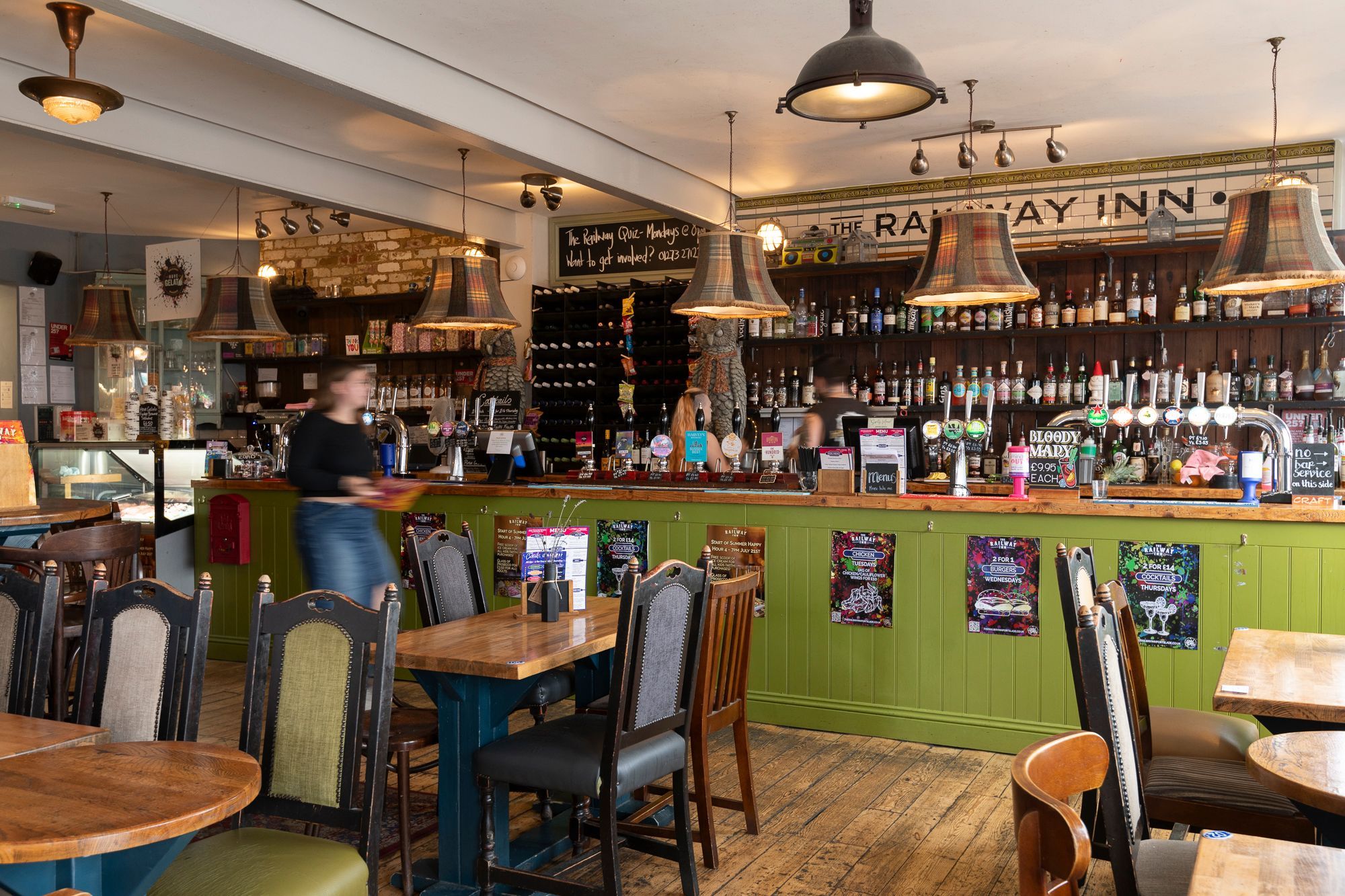 interior shot of The Railway Inn pub. Wooden chairs and tables, green bar area, lots of drinks