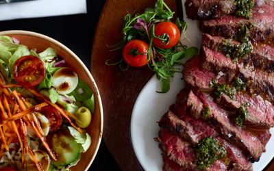 overhead shot of the medium rare steak and cherry tomatoes on a vine. The steak is on a white plate on a wooden table. there is another dish which is out of shot. LatinoAmerica is a Brighton steak restaurant situated in Hove on Church Road.