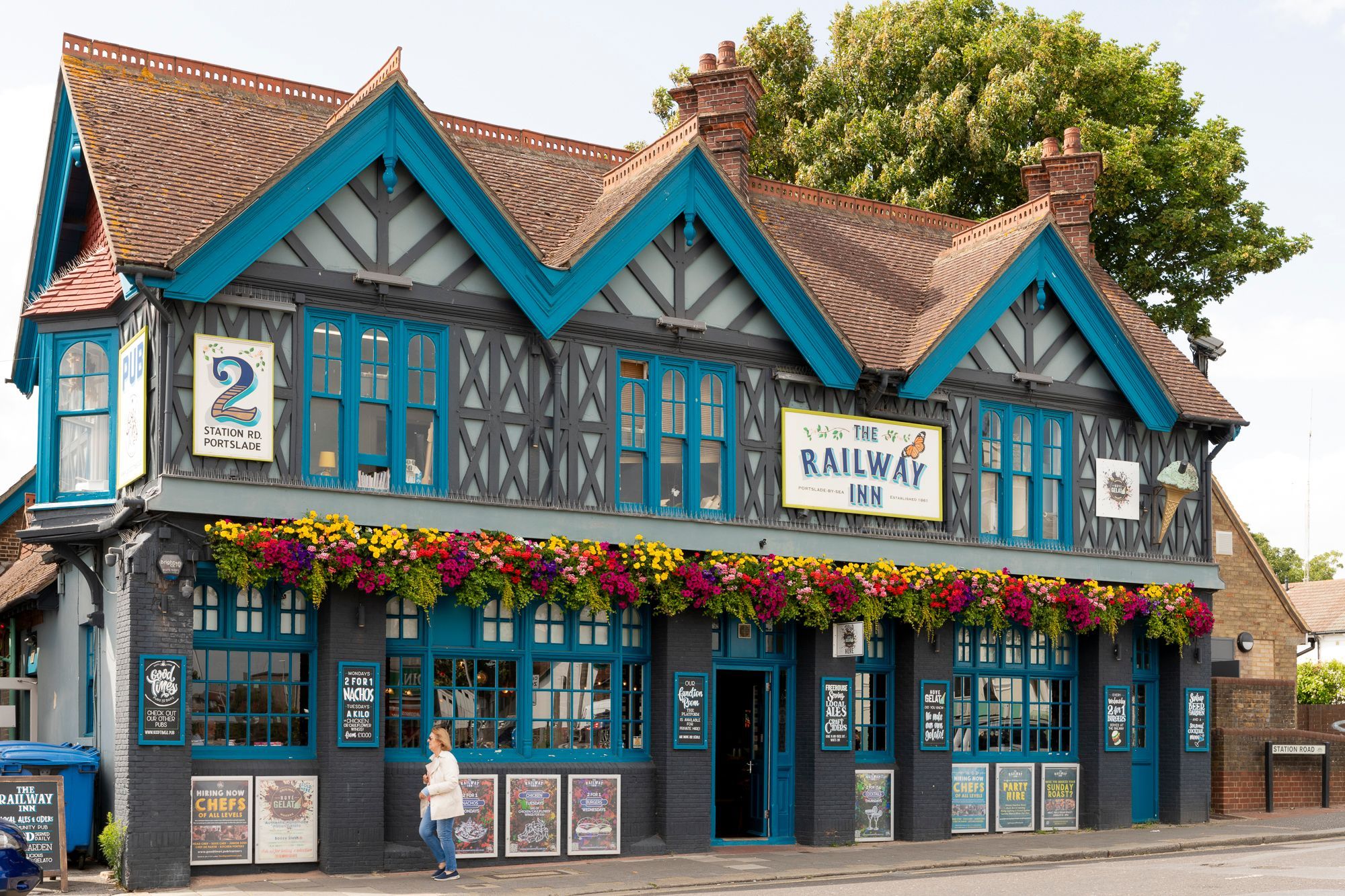 exterior shot of the The Railway Inn pub. Blue and grey wall with lots of flowers as decoration.