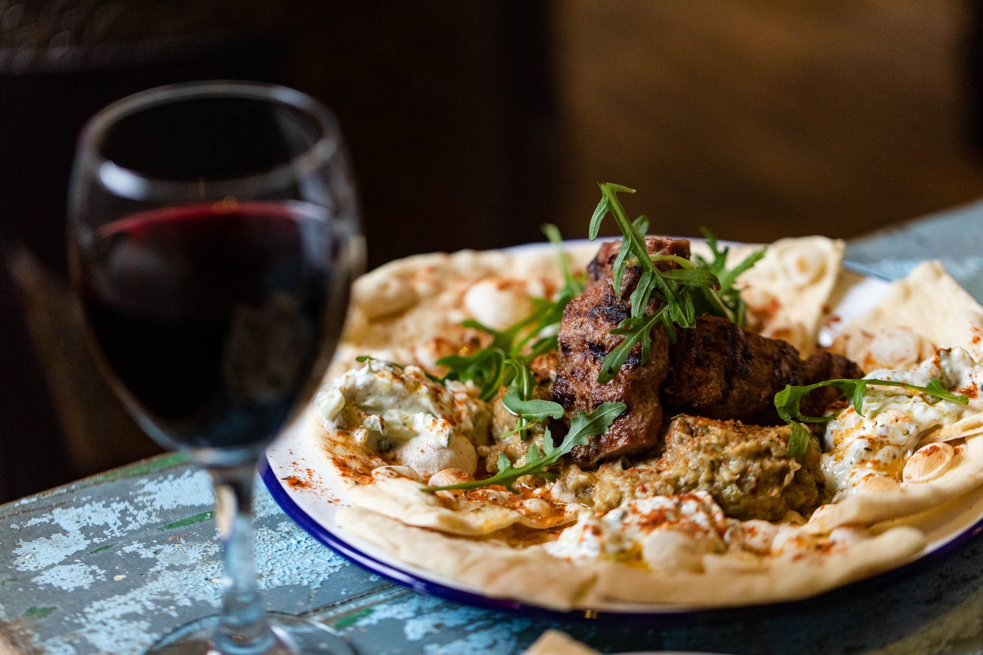 side shot of the some sort of meat served with thin and crusty bread and glass of wine