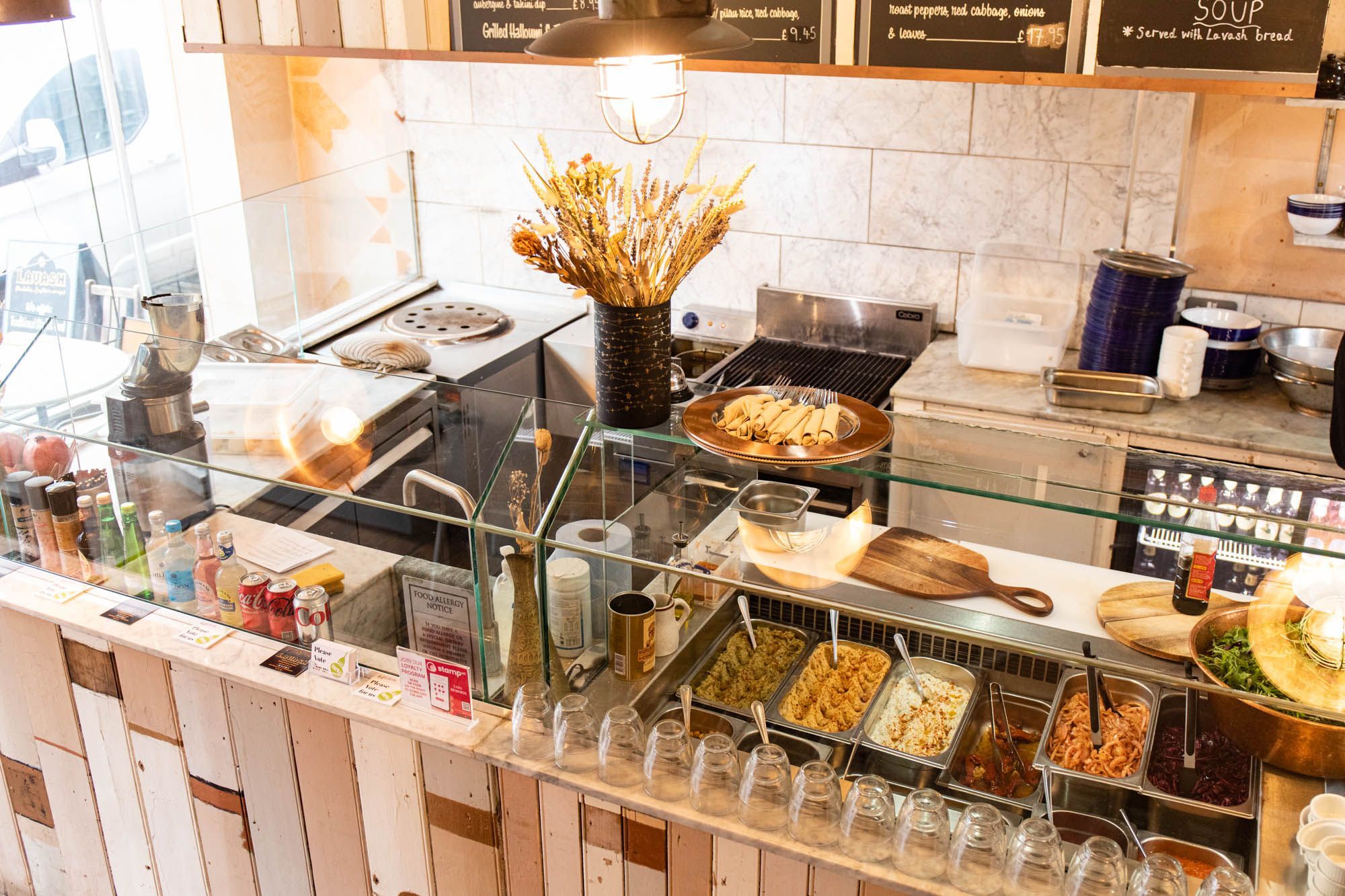 over head shot of the food bar area of Lavash Brighton, different type of ingredients in metal bowls, different sauces and drinks in fridge