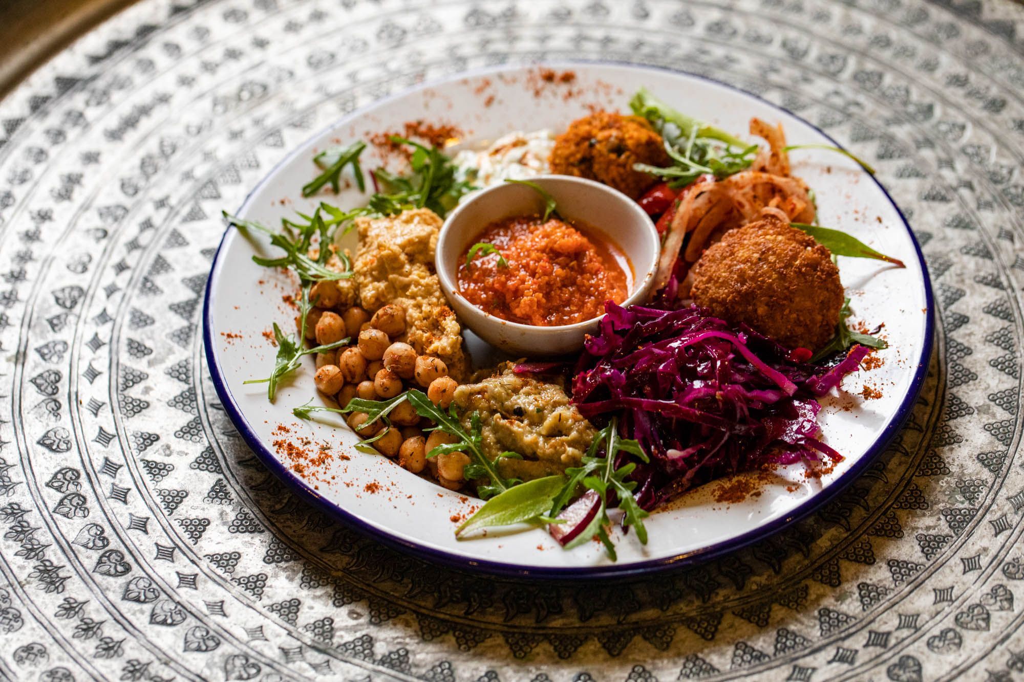 colorful looking plate with purple cabbage, some chickpeas, falafel and orange sauce served in white plate at Lavash Brighton