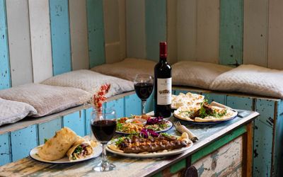 wooden table at the Lavash laid out with multiple Middle Eastern dishes served with bottle of red wine, two glasses filled with red wine