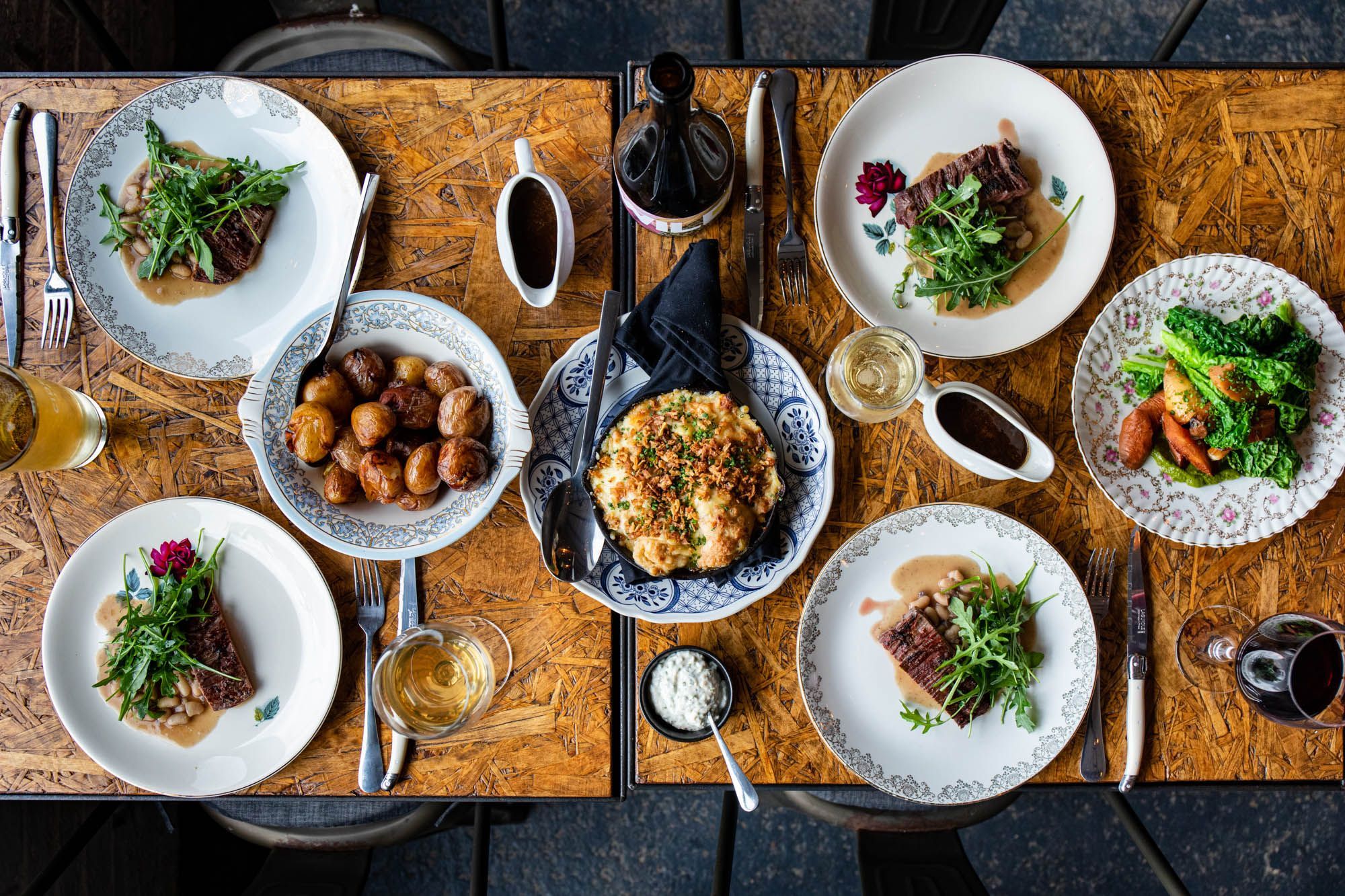two brown tables at Cider Tap connected and laid out with seven different dishes, red wine, beer and gravy 