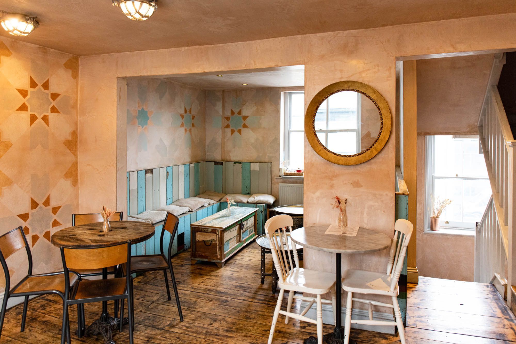 top floor of the Lavash Brighton, two different coloured tables, one is white with white chairs, other one is brown with brown chairs, there is a corner blue and white seating with wooden table. Walls are beige and with some decorations on them