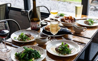 The Cider Tap Sussex window table laid out with four main dishes and two sides with glass of beer, wine and bottle of red wine