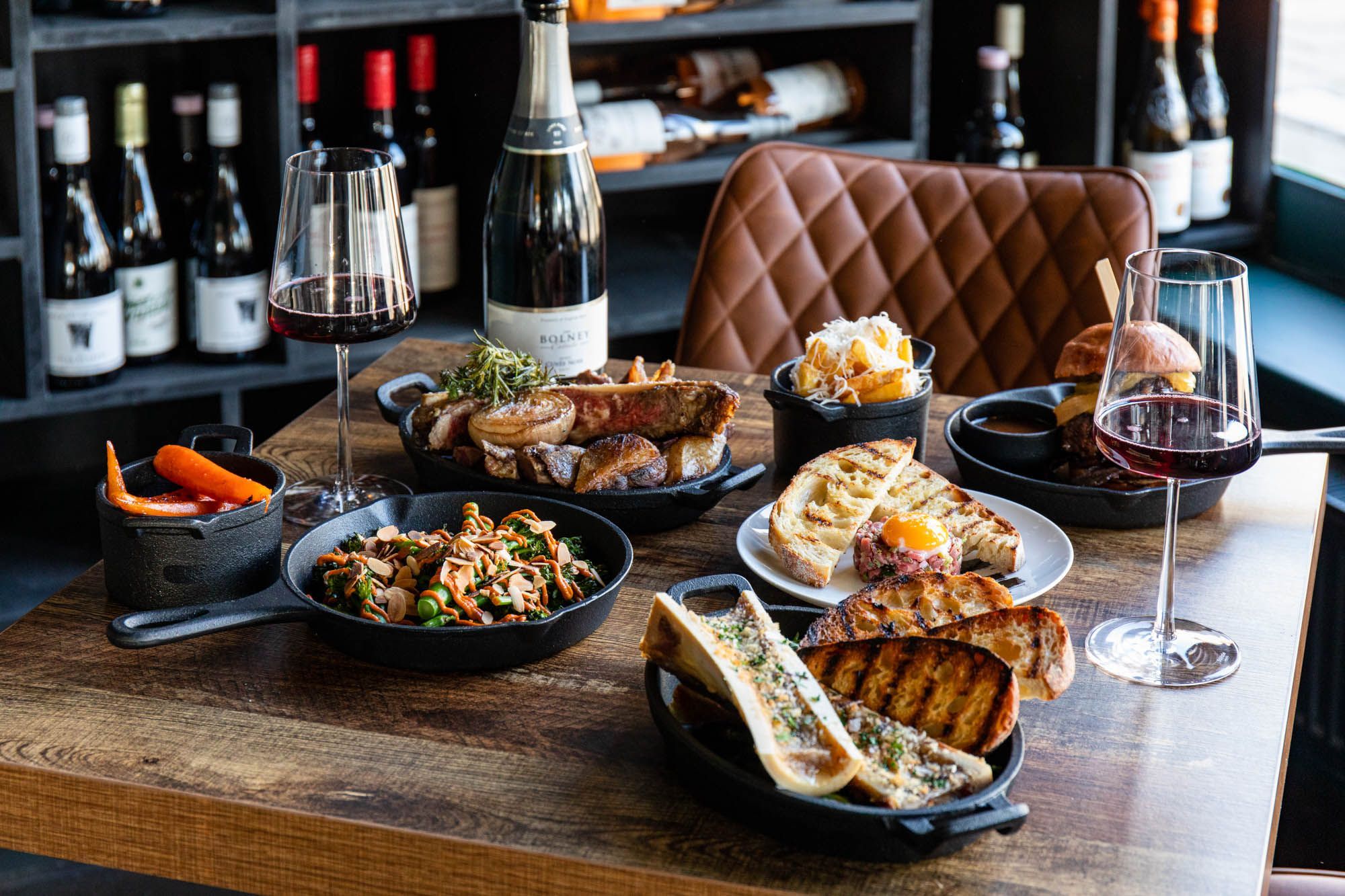 side shot of the brown table laid out with couple of different meat dishes and sides, with bottle of red sparkling wine 