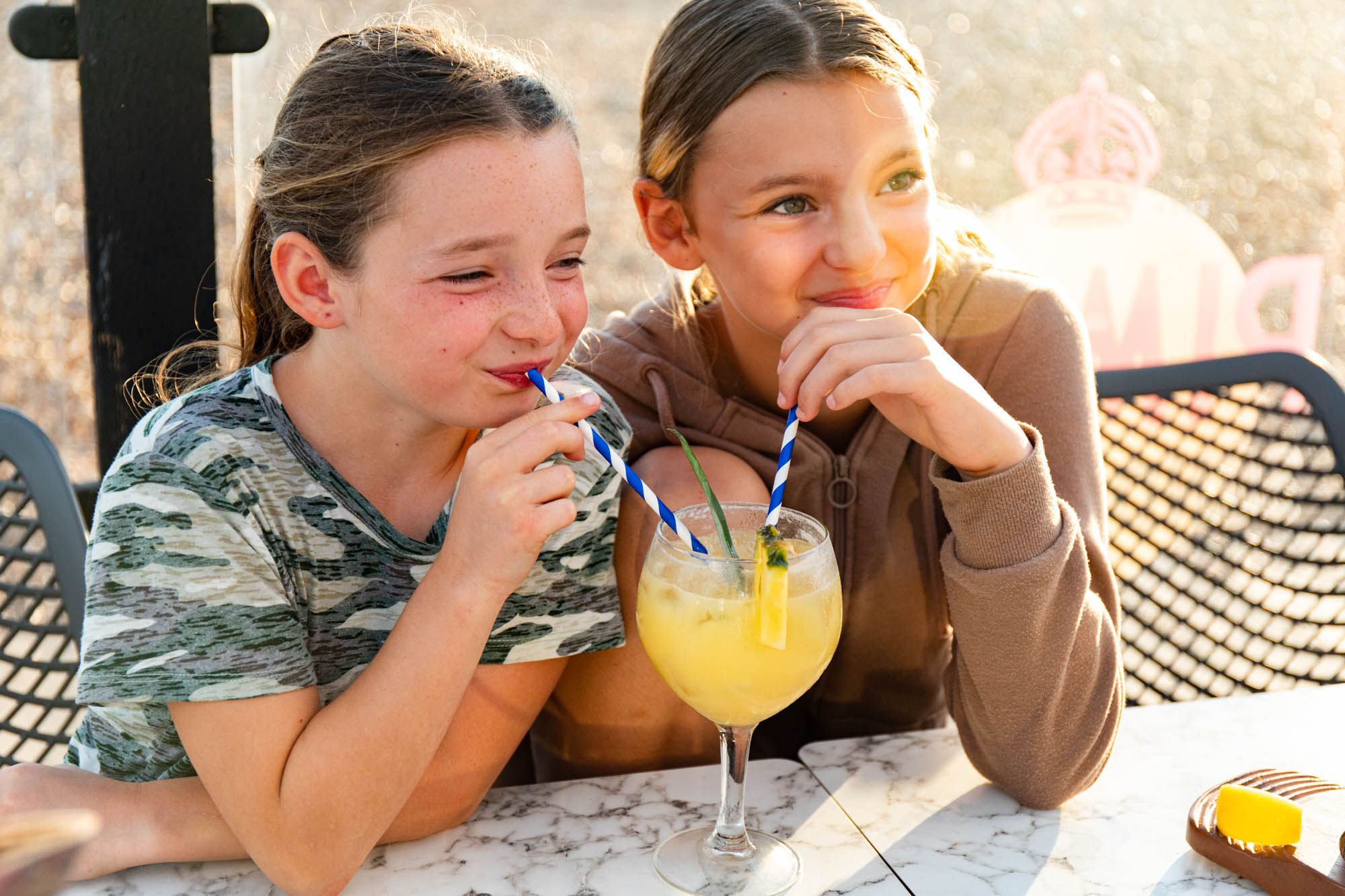 Two girls sharing a drink on the beach on a sunny day.