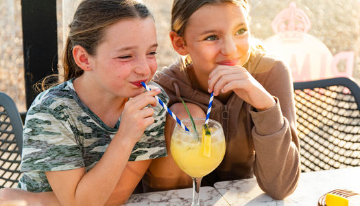 Two girls sharing a drink on the beach on a sunny day.
