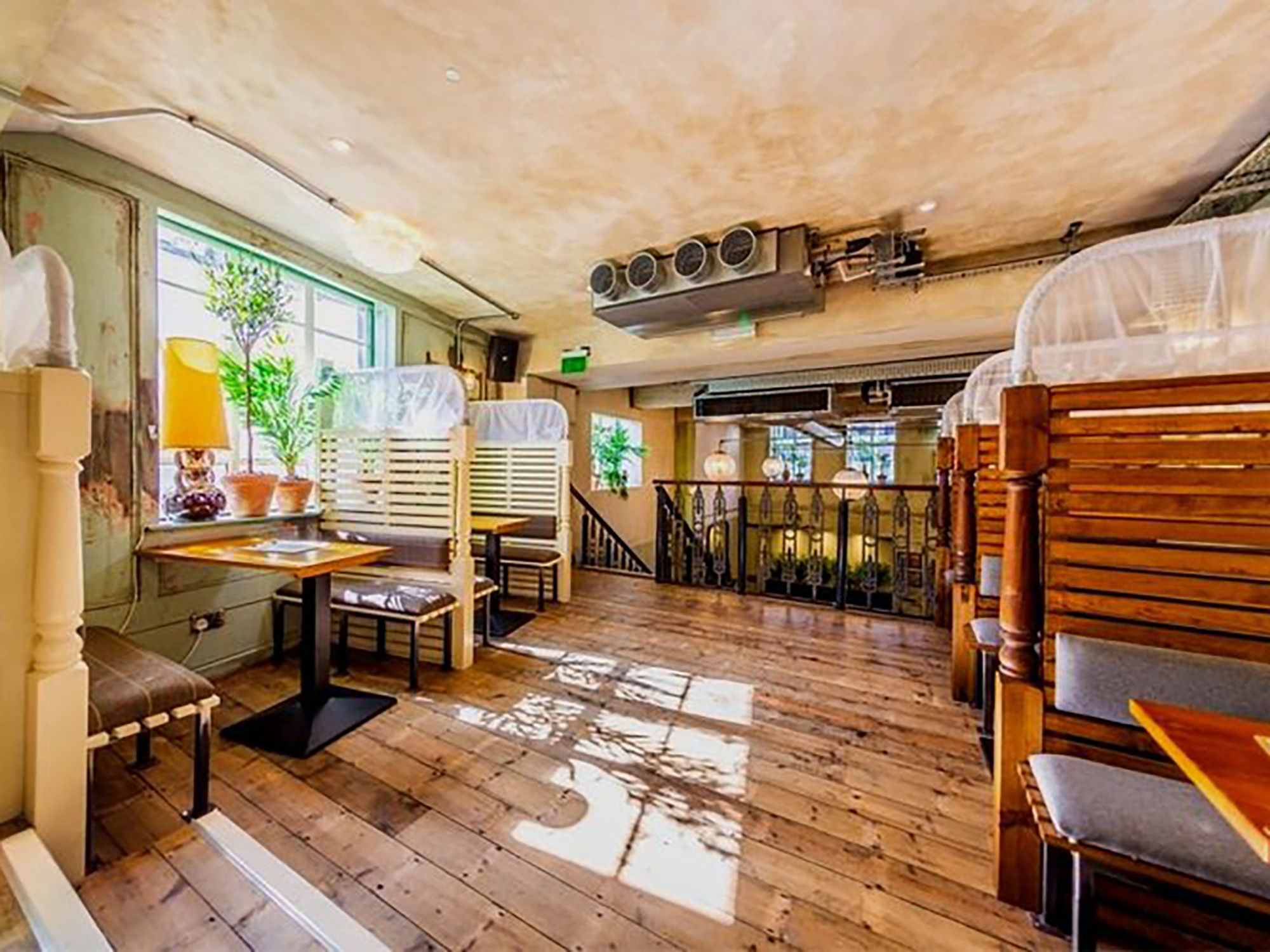 The mezzanine area at Oculist Brighton with sun shining through the windows and rustic wooden interiors. Booth style tables and chairs with cushioned seating. 