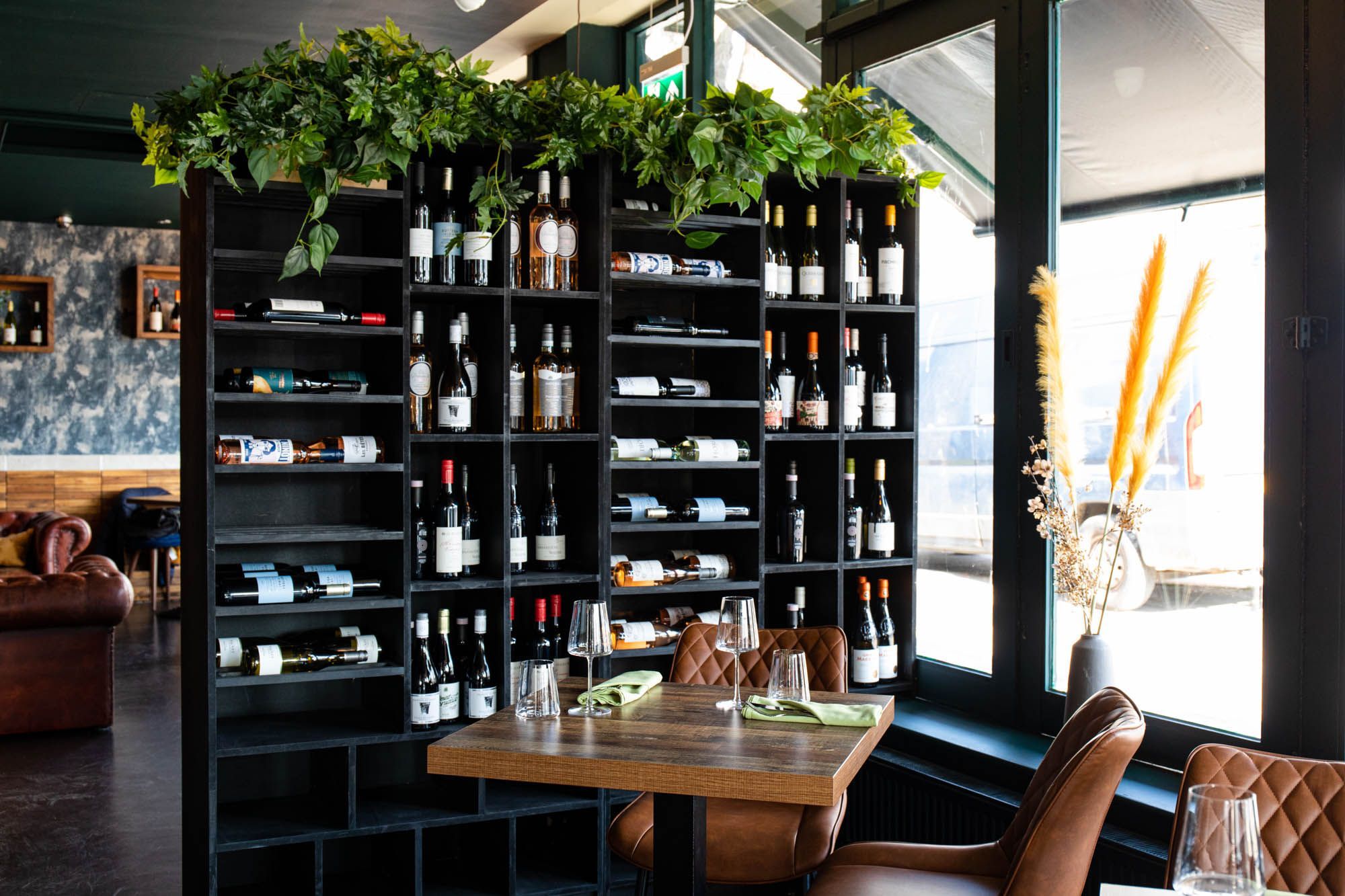 Black shelf unit filled with various quality wines at the restaurant Carne in Hove, small brown table and chairs situated next to eat and set to be served with food
