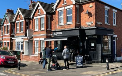 Exterior photography of 44 Poets on a sunny day with a blue sky. People are walking past and there's a red car parked outside.