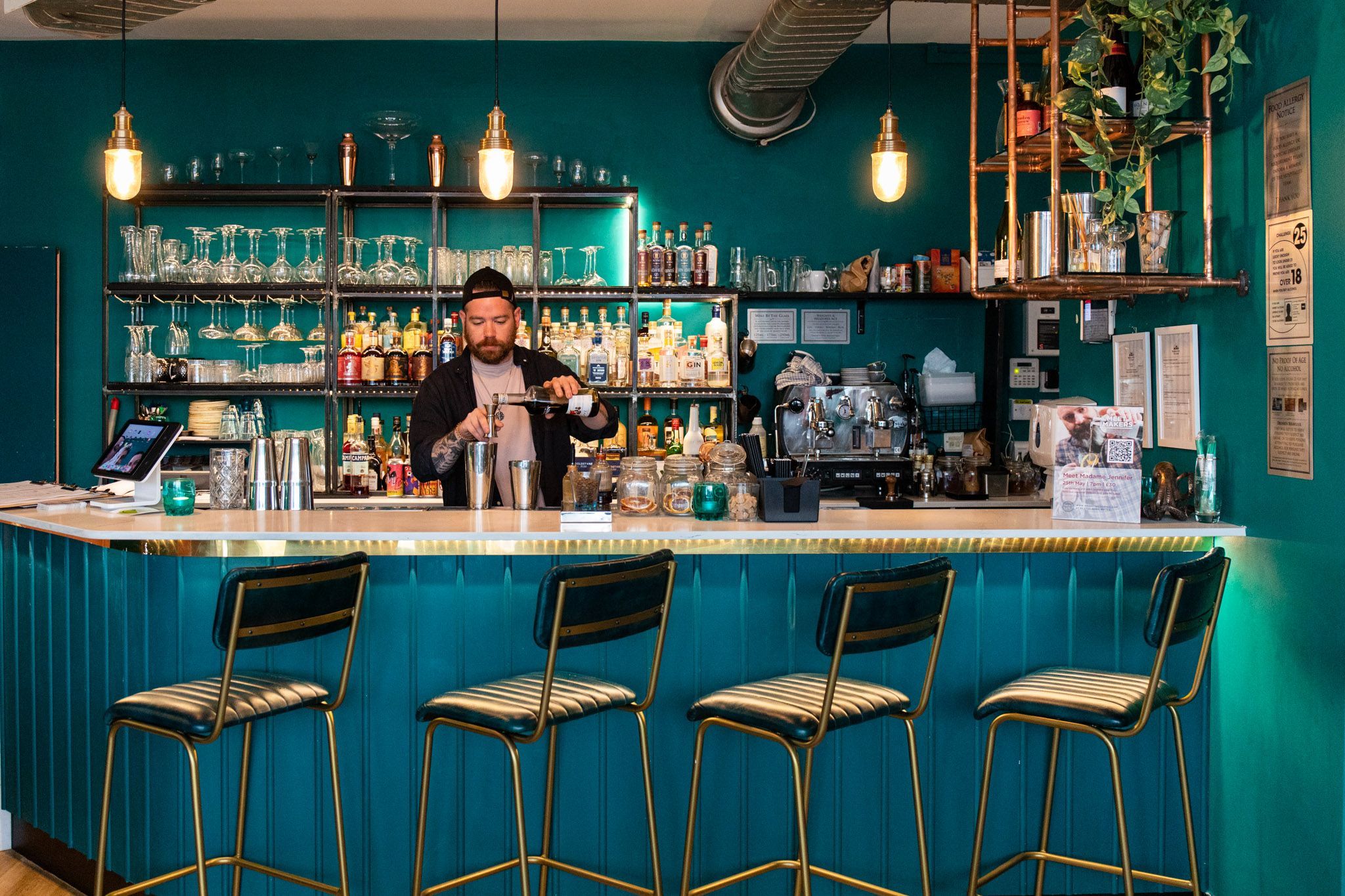 Brighton Cocktail Company bar area coloured in teal, nice black bar chairs and bartender preparing cocktails