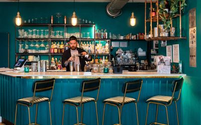 Brighton Cocktail Company bar area coloured in teal, nice black bar chairs and bartender preparing cocktails. Part of our Brighton nightlife guide