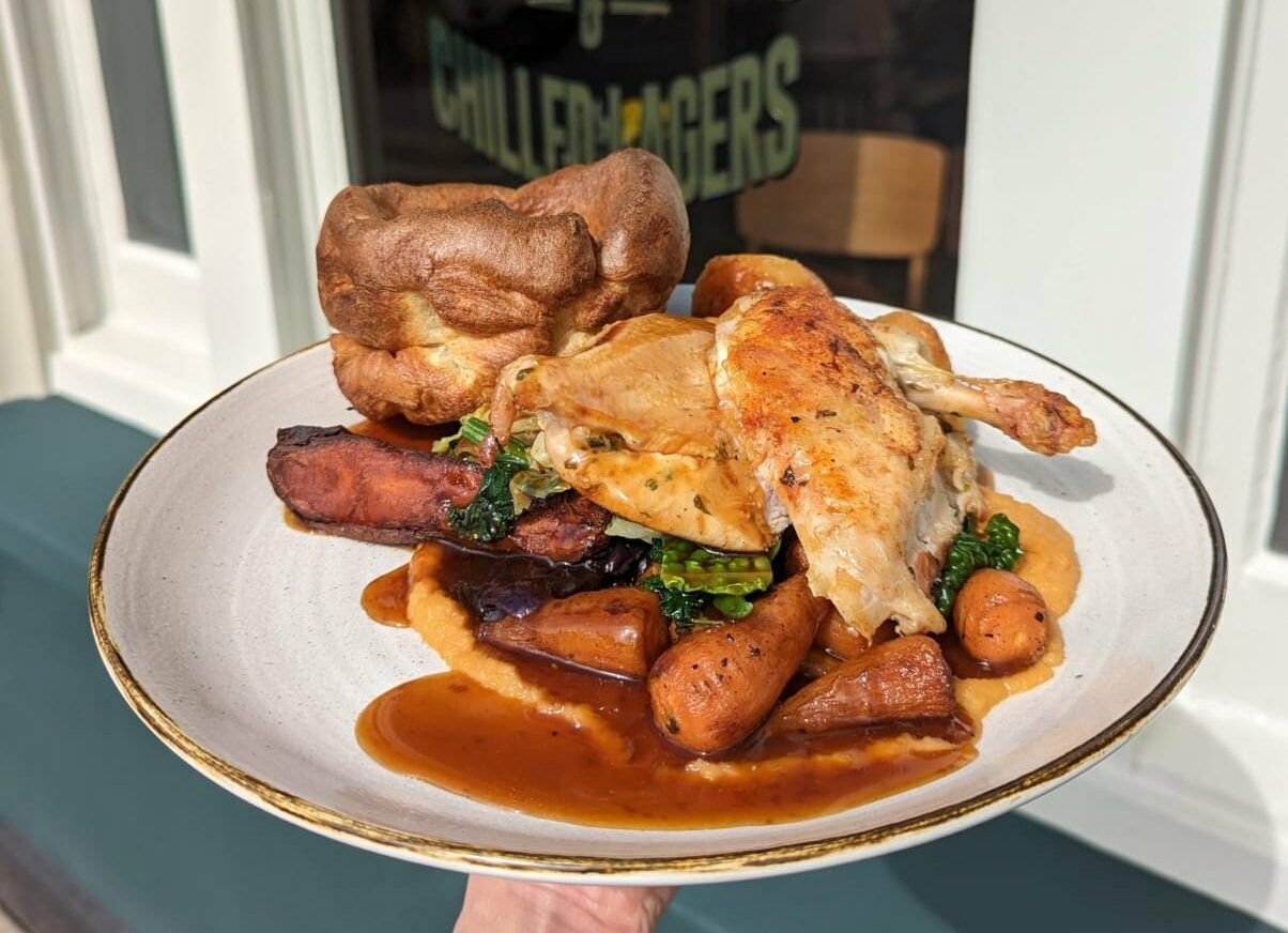Hand holding mouth watering Sunday Roast on the white plate at The Cricketers Worthing