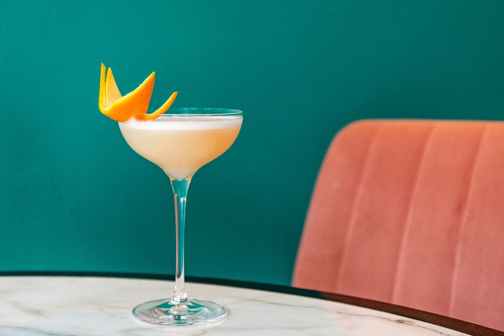 orange cocktail on the marble table with the wall coloured in teal background and peach seating