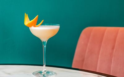 orange cocktail on the marble table with the wall coloured in teal background and peach seating