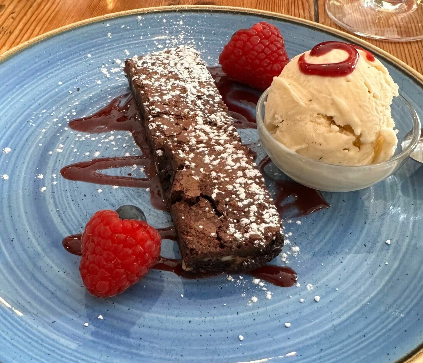 Chocolate brownie with two strawberries and ice cream served on blue plate