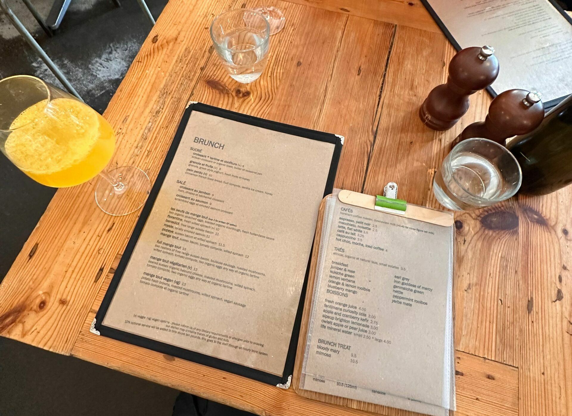 over head shot of the food and cocktail menu on the wooden table and glass of the mimosa drink next to it