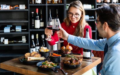 couple having a toast with glasses of red wine above their brown table laid out with various meat dishes at Carne Hove