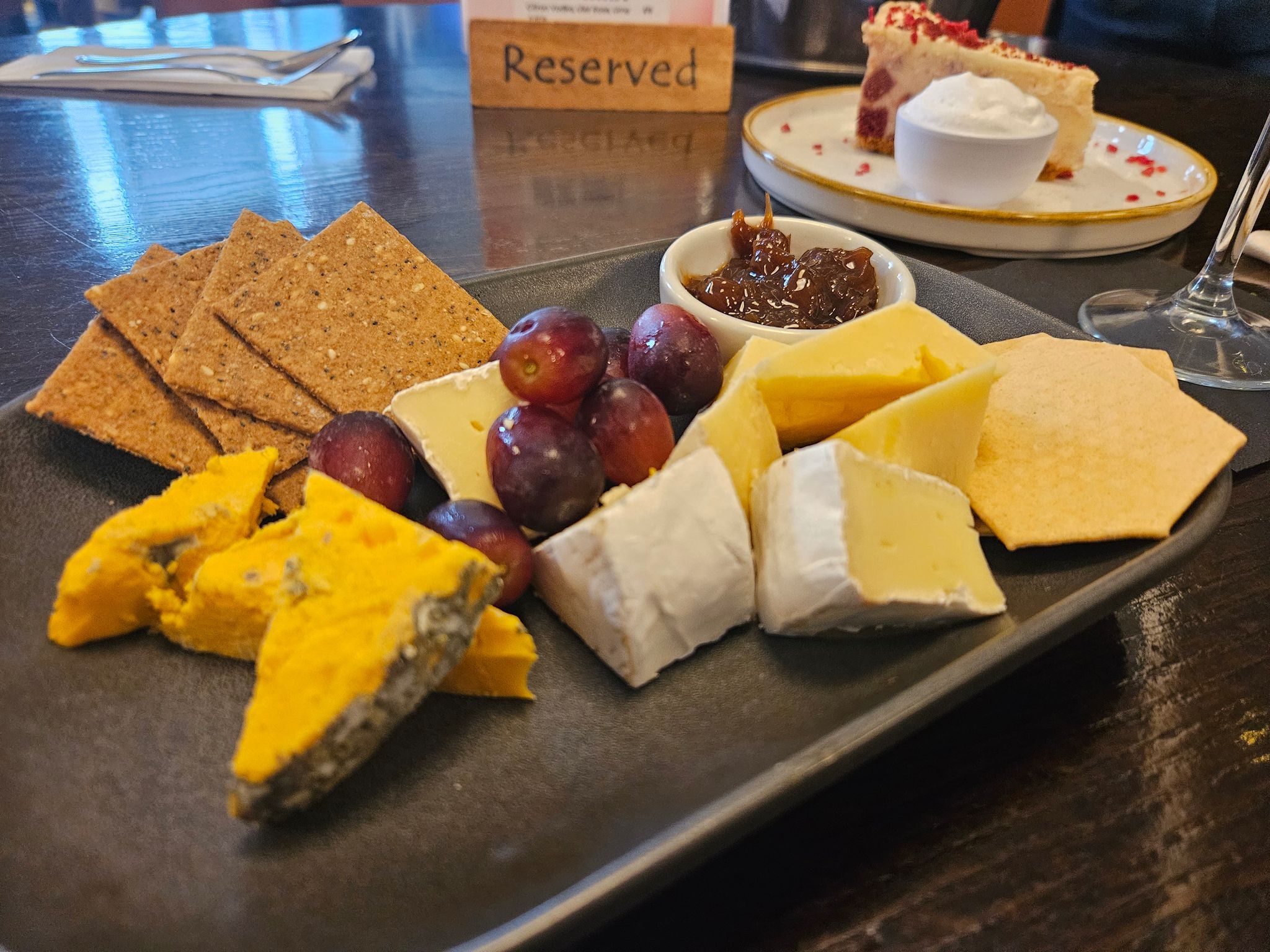 charcuterie board on the table, crackers, grapes, cheese and chutney served on black board