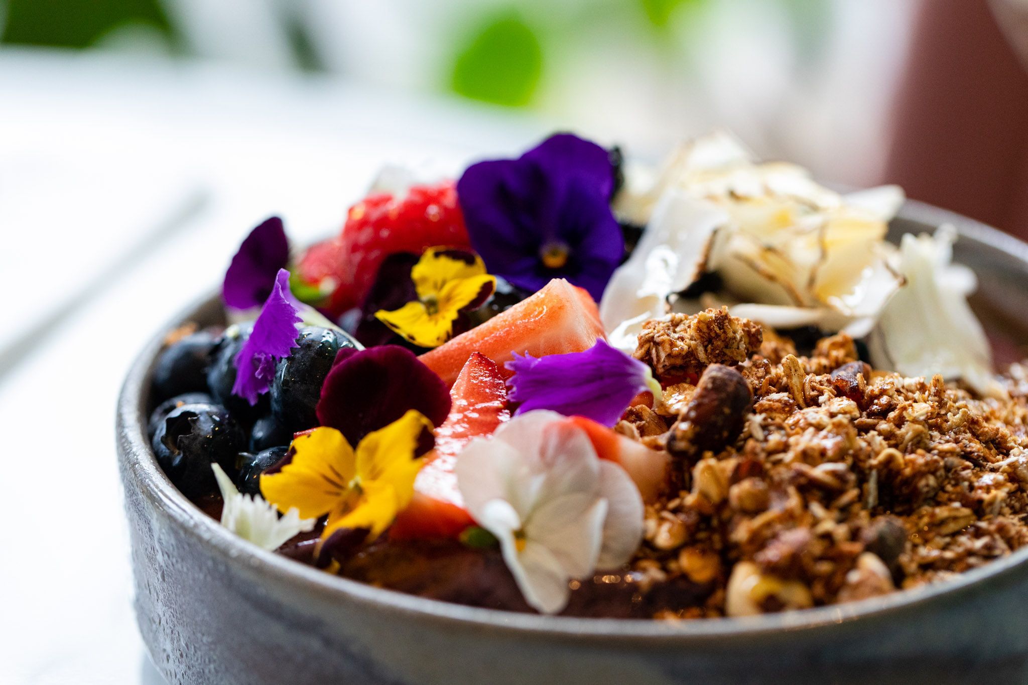 close up shot of the grey bowl filled with granola, fruits, and small flowers as decoration