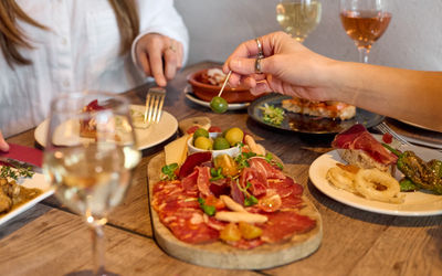 Antipasti at Tinto Taperia with a selection of meats on a chopping board. There's a bowl of mixed olives with two women eating food. Two glasses of white wine are on the table.
