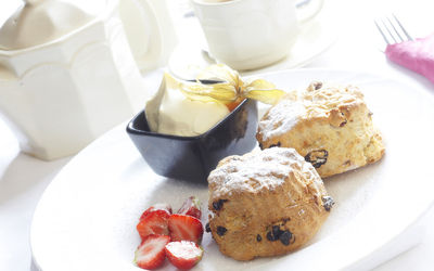 Scones and a pot of clotted cream on a white plate with sliced strawberries and a cup of tea at The Old Tollgate Hotel in Steyning.