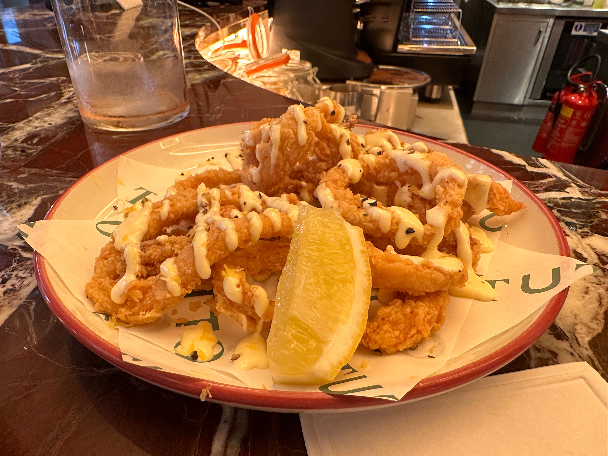 Crispy calamari rings piled on a plate with a wedge of lemon and a drizzle of creamy sauce.