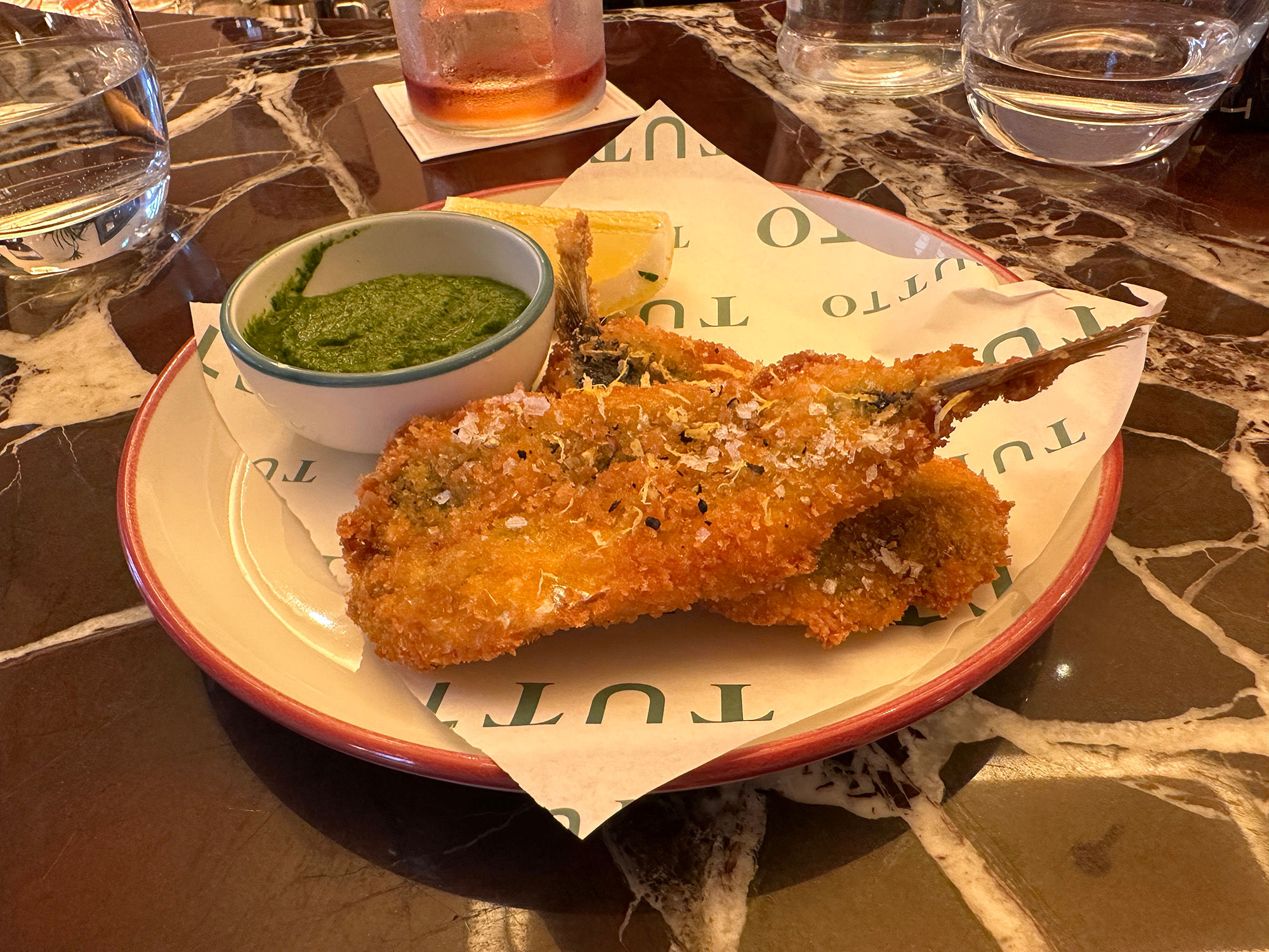 A plate of sardines with a herb dip served on a small plate with Tutto branded paper for the Italian sharing menu.