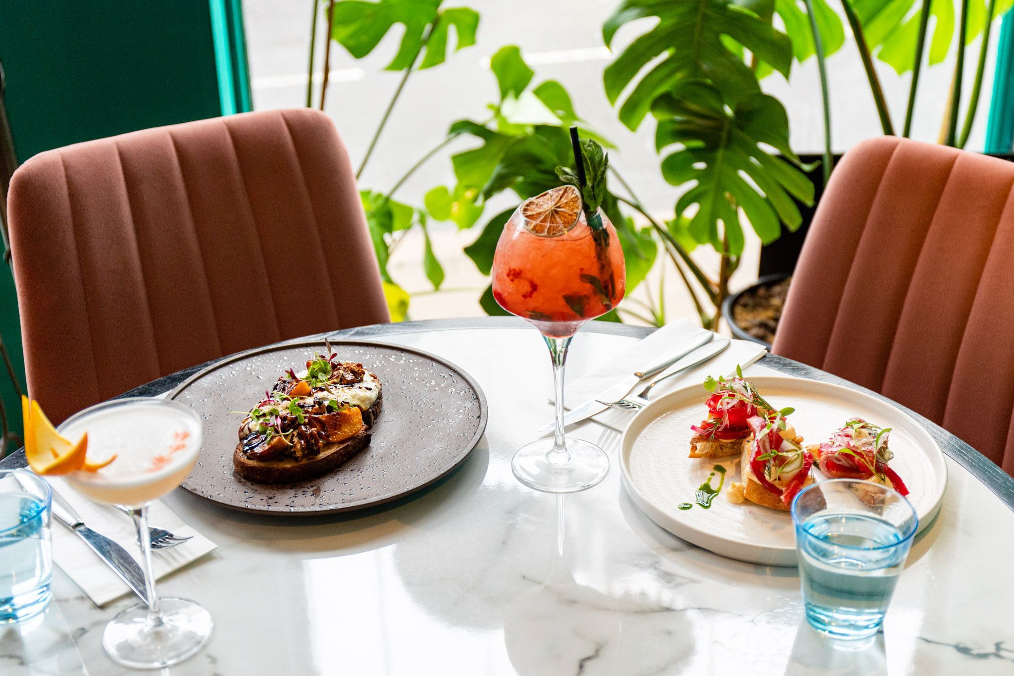 two brunch dishes served on the marble table and with two different cocktails at Brighton Cocktail Company