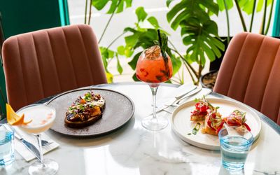 two brunch dishes served on the marble table and with two different cocktails at Brighton Cocktail Company
