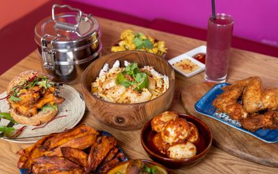 wooden brown table laid out with Nanima Brighton dishes including plantain, fried chicken, burger, fries, dumplings