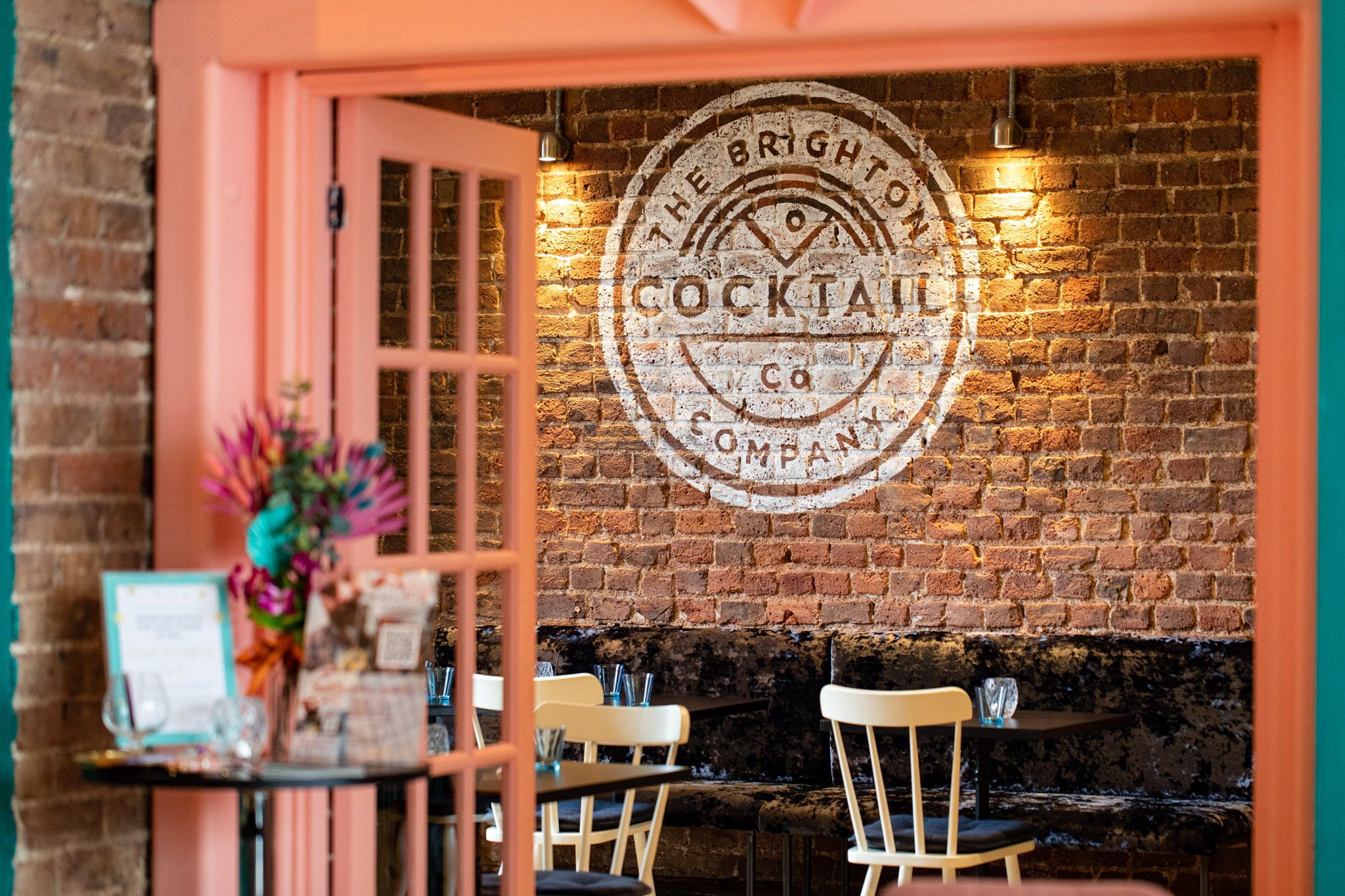 shot of Brighton Cocktail Company white logo on the orange brick wall