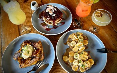 over head shot of the brunch at the Mesmerist, including American pancakes with syrup, banana sweet dish, three different cocktails. Bottomless brunch Brighton