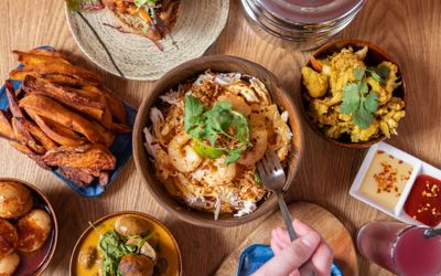 over head shot of the wooden brown table laid out with Nanima Brighton dishes including plantain, fried chicken, burger, fries, dumplings