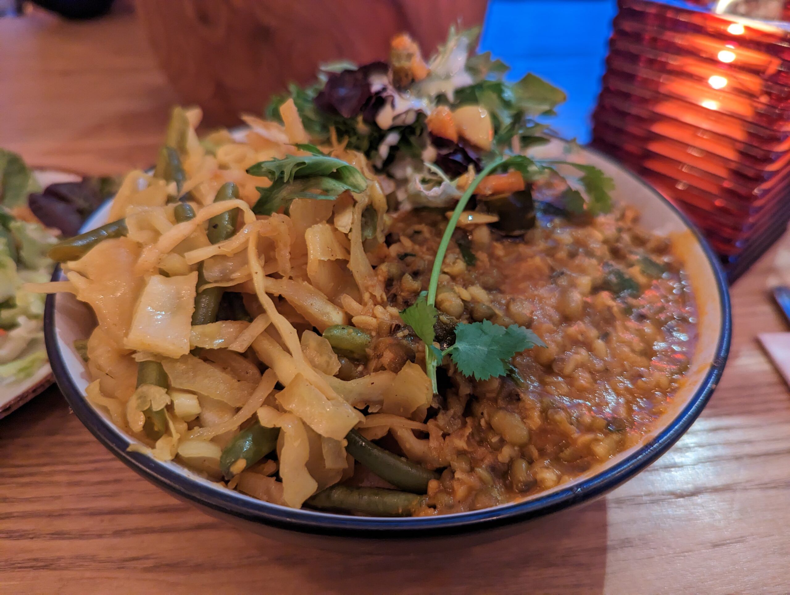 a mixed bowl of the tarka daal, rice, and a veg side of Malaysian cabbage and green beans served in white bowl as a part of dinner in Kemptown