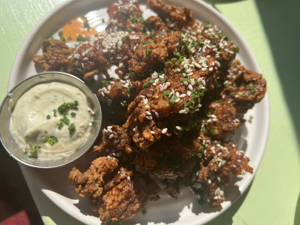 Sticky chicken bites for an Oeuf experience at the Hove cafe. Served on a plate on a green table.