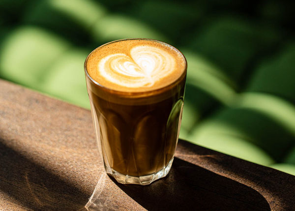 A glass of coffee with the sunlight shining on the table and green chair in the background at White Cloud Coffee.