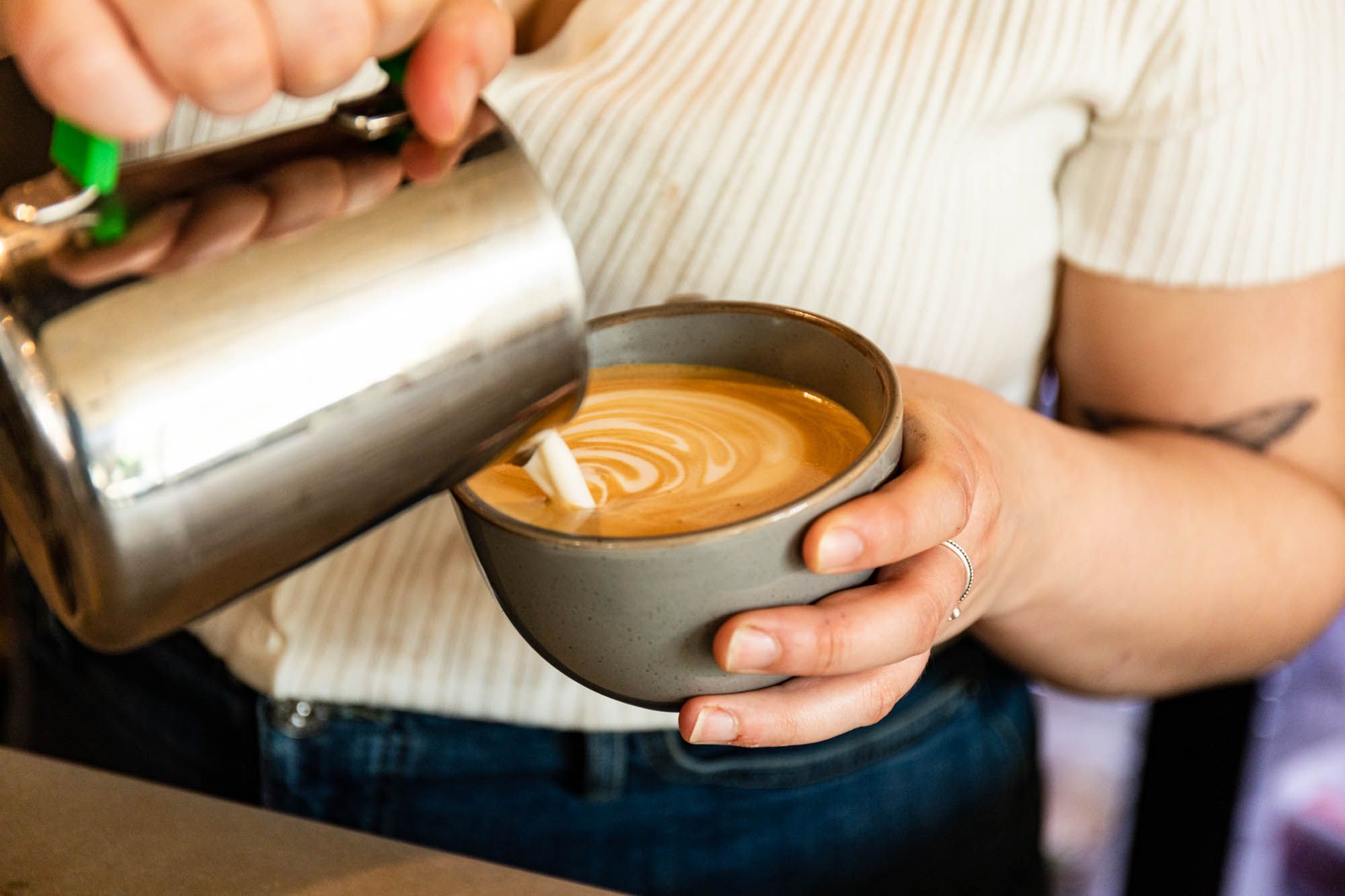 bartender holding cup of coffee and making coffee art with milk 