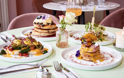 A selection of brunch dishes served on a decadent wooden table painted light green with a small glass vase in the middle of the table with roses. Oeuf Cafe in Hove are the winners of the best brunch in Brighton in the 2024 Brighton Restaurant Awards.